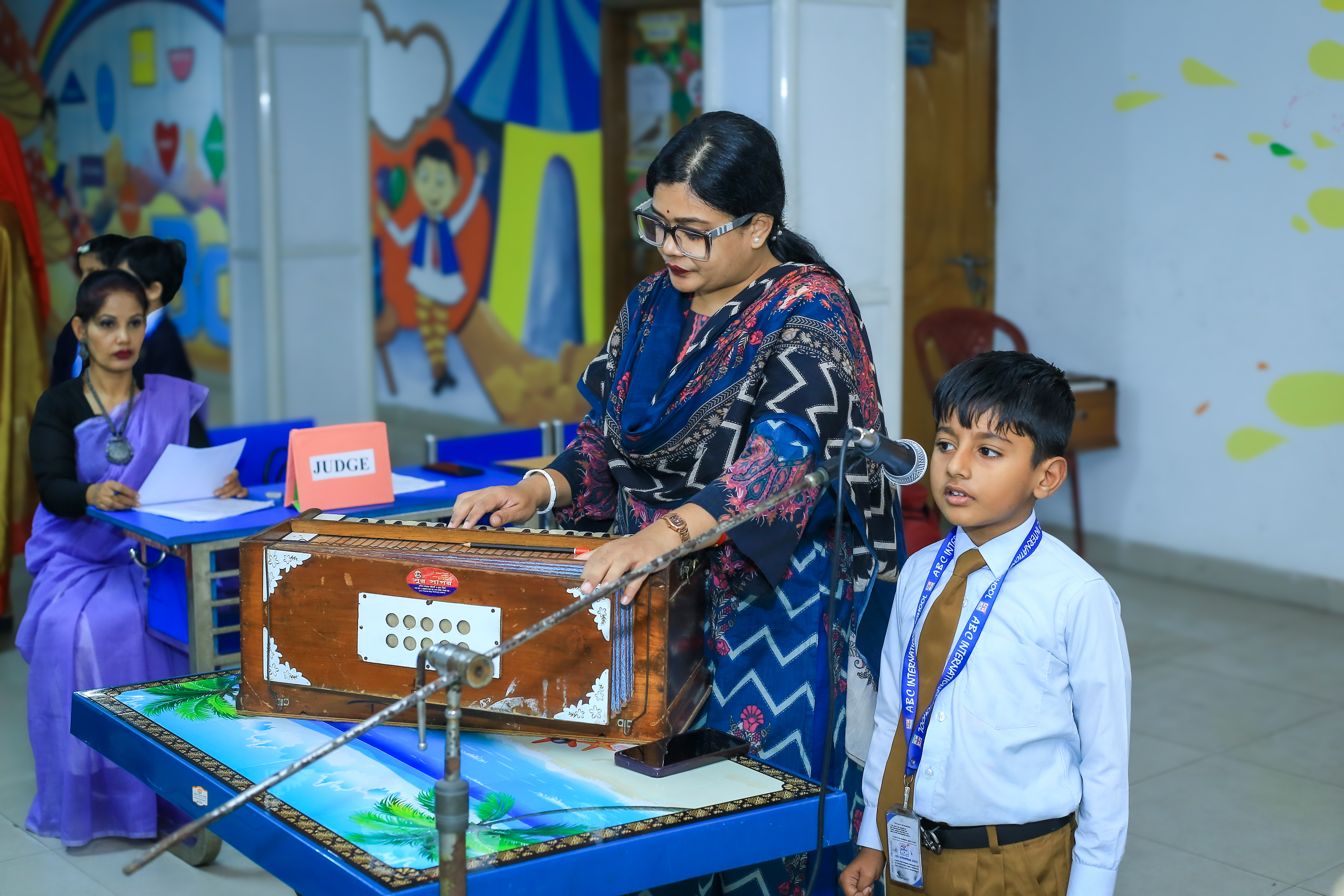A student and a teacher standing beside the harmonium during a festival performance